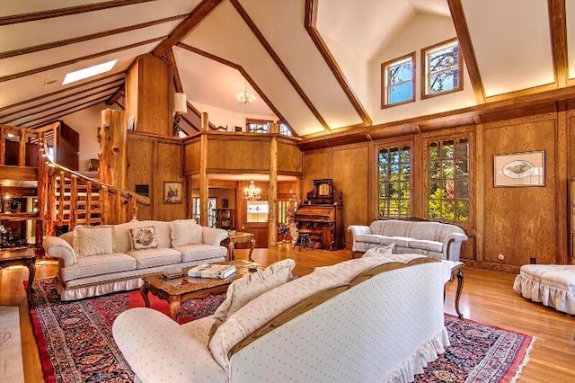 living room with a chandelier, high vaulted ceiling, light hardwood / wood-style flooring, wood walls, and a skylight