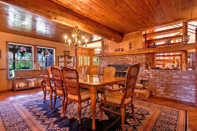 dining space featuring beamed ceiling, wooden ceiling, hardwood / wood-style floors, a brick fireplace, and a chandelier