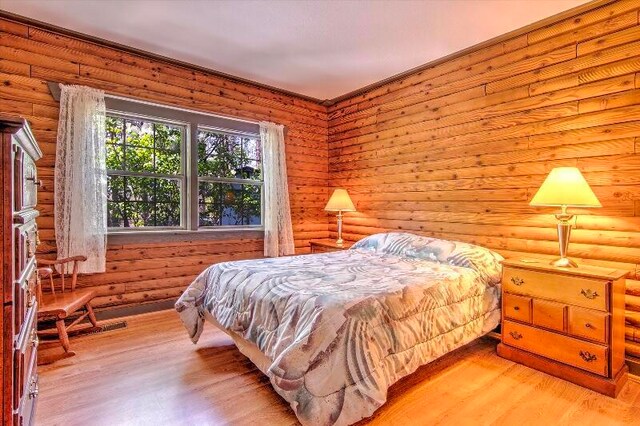 bedroom featuring log walls and light hardwood / wood-style flooring