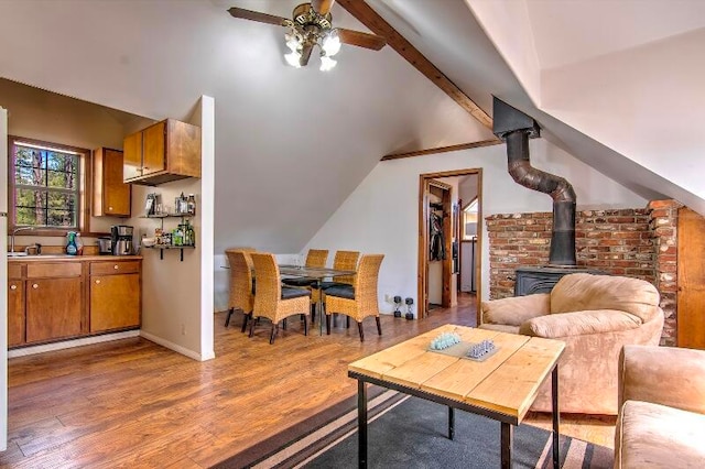 living room featuring light hardwood / wood-style floors, vaulted ceiling with beams, a wood stove, and ceiling fan