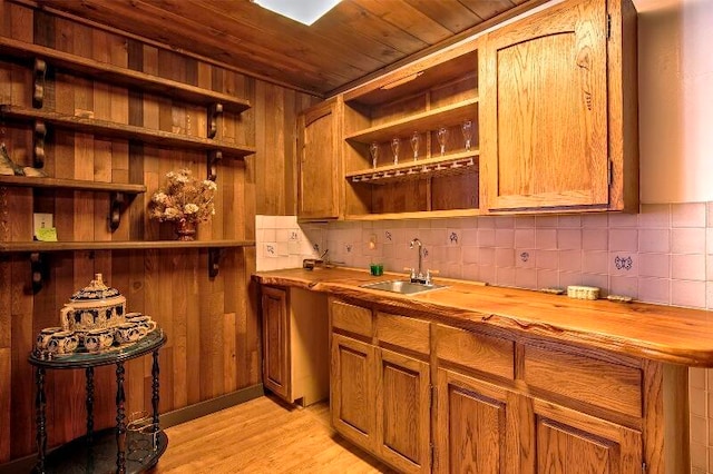 bar with wooden counters, sink, light wood-type flooring, and wooden walls