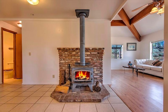 living room featuring beam ceiling, light hardwood / wood-style flooring, a wood stove, and ceiling fan