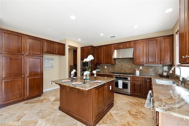 kitchen featuring backsplash, a kitchen island with sink, sink, appliances with stainless steel finishes, and light stone counters