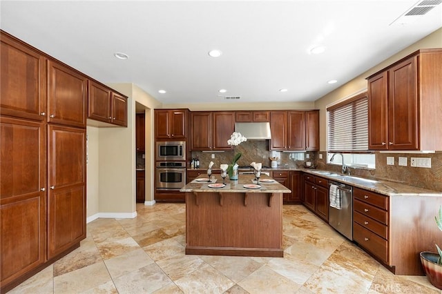 kitchen with sink, decorative backsplash, light stone countertops, appliances with stainless steel finishes, and a kitchen island