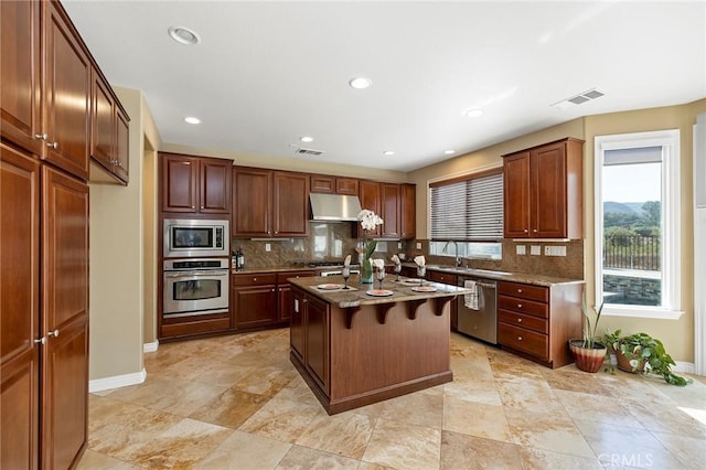 kitchen featuring decorative backsplash, a breakfast bar, stainless steel appliances, a center island with sink, and stone counters