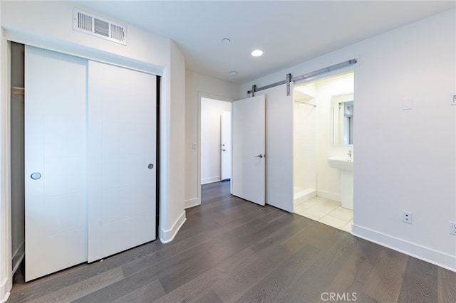 unfurnished bedroom featuring sink, a barn door, hardwood / wood-style floors, connected bathroom, and a closet