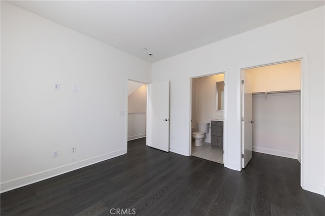 unfurnished bedroom featuring a closet, ensuite bath, a spacious closet, and dark wood-type flooring