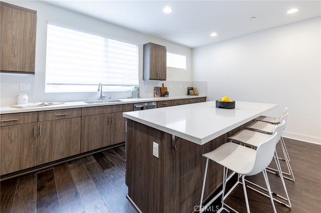 kitchen with sink, stainless steel dishwasher, dark hardwood / wood-style floors, a kitchen island, and a breakfast bar area