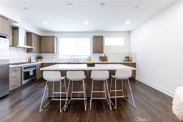 kitchen featuring dark hardwood / wood-style flooring, a kitchen island, wall chimney range hood, and appliances with stainless steel finishes