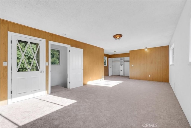 unfurnished living room featuring light carpet, wood walls, and a textured ceiling