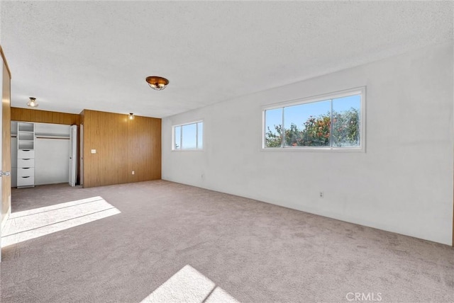 unfurnished living room with light carpet, a wealth of natural light, and wood walls