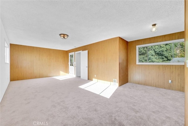 carpeted empty room with a textured ceiling and wooden walls