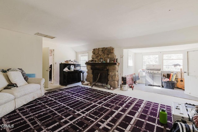 living room with visible vents, a stone fireplace, and vaulted ceiling