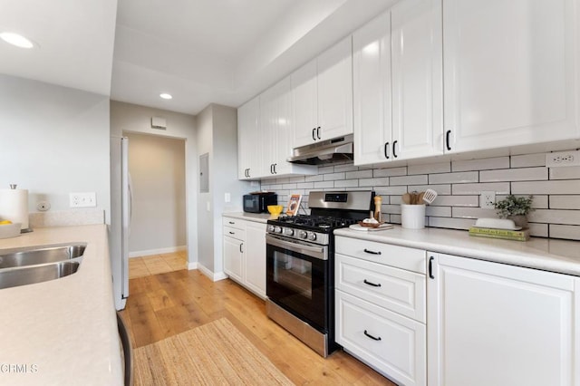 kitchen featuring stainless steel gas range oven, backsplash, white cabinets, sink, and light hardwood / wood-style flooring