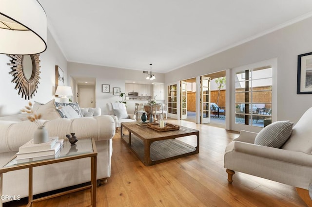 living room with light hardwood / wood-style floors, crown molding, and an inviting chandelier