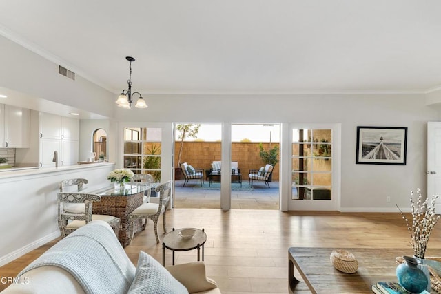 living room with a chandelier, light wood-type flooring, and ornamental molding