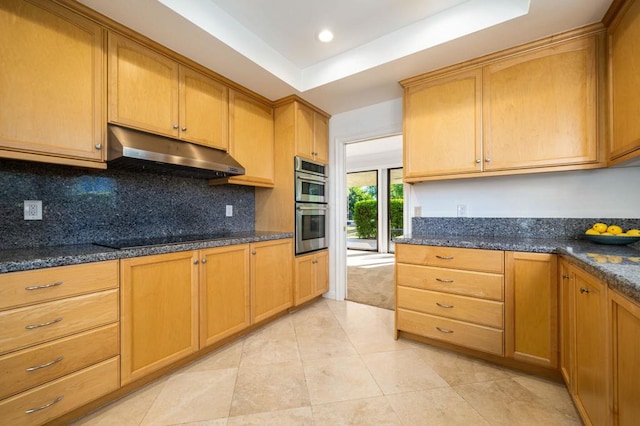 kitchen featuring double oven, dark stone countertops, black stovetop, and a tray ceiling