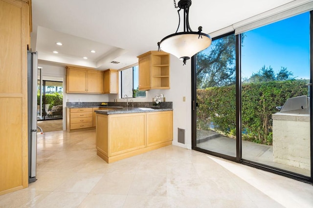 kitchen with a raised ceiling, sink, light brown cabinetry, decorative light fixtures, and kitchen peninsula