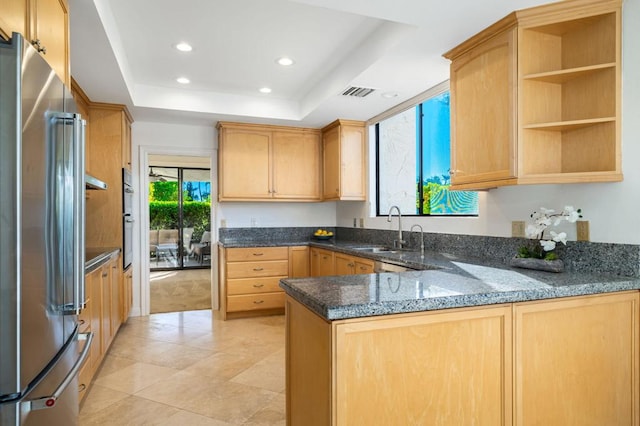 kitchen with sink, dark stone countertops, appliances with stainless steel finishes, a tray ceiling, and kitchen peninsula