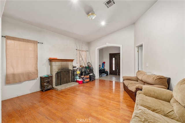 living room with a tiled fireplace, wood-type flooring, and vaulted ceiling