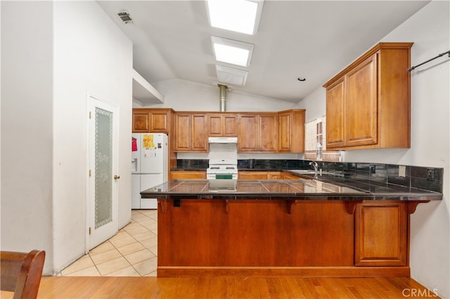 kitchen featuring lofted ceiling, kitchen peninsula, white appliances, a kitchen bar, and light hardwood / wood-style floors