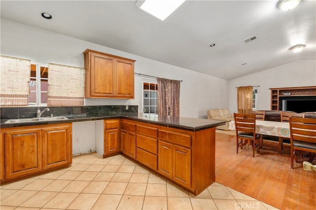 kitchen featuring kitchen peninsula, sink, light wood-type flooring, and vaulted ceiling