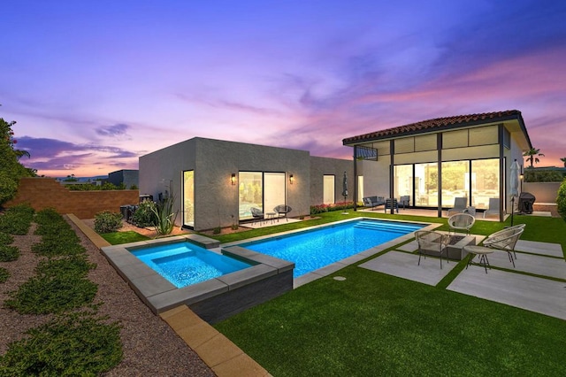 pool at dusk featuring an in ground hot tub, a patio, and a yard