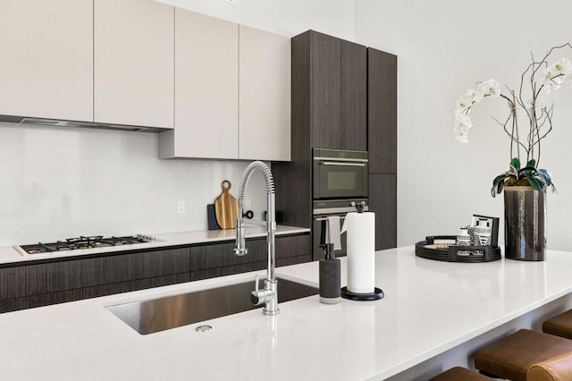 kitchen with sink, white gas cooktop, a kitchen breakfast bar, white cabinetry, and dark brown cabinetry