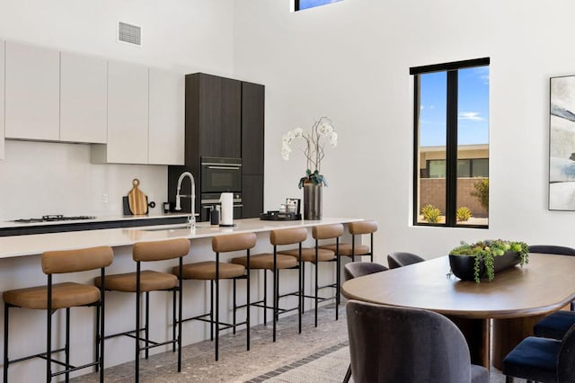 kitchen featuring gas cooktop, white cabinetry, wall oven, and a kitchen bar