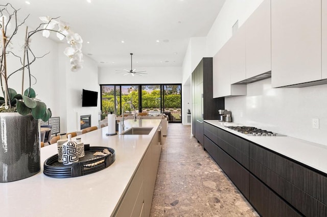 kitchen with stainless steel gas stovetop, white cabinets, sink, and ceiling fan