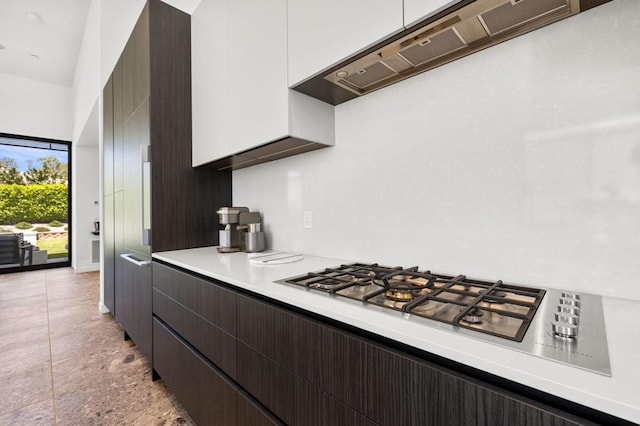 kitchen featuring stainless steel gas stovetop, dark brown cabinetry, exhaust hood, and white cabinets