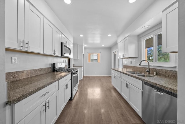 kitchen with dark wood-type flooring, white cabinets, sink, dark stone countertops, and appliances with stainless steel finishes