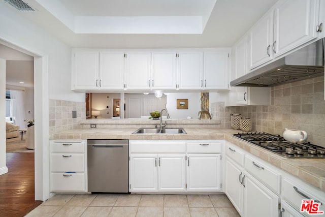 kitchen with sink, tile countertops, light hardwood / wood-style floors, white cabinets, and appliances with stainless steel finishes