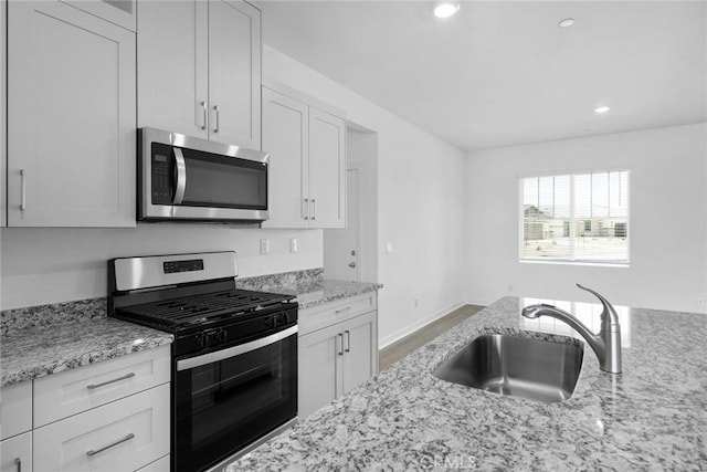 kitchen featuring sink, appliances with stainless steel finishes, light stone counters, and white cabinetry