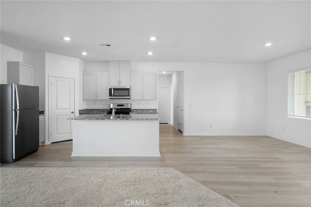 kitchen with stone countertops, a kitchen island with sink, white cabinets, appliances with stainless steel finishes, and light hardwood / wood-style floors