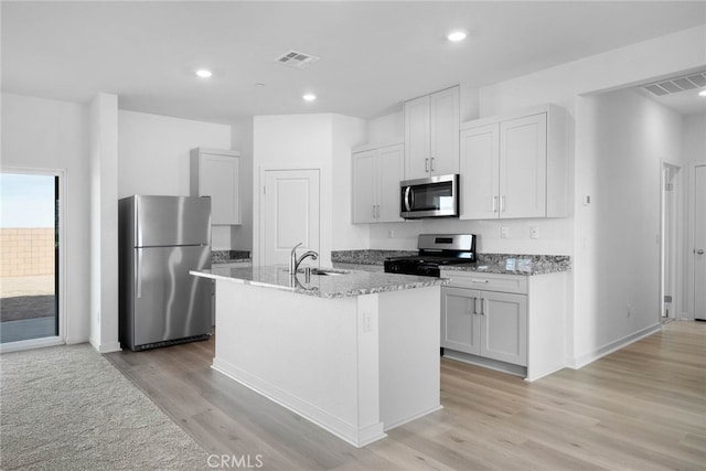 kitchen with sink, light wood-type flooring, white cabinetry, stainless steel appliances, and a kitchen island with sink