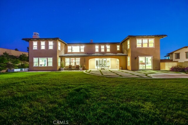 back house at twilight featuring a patio area, an outdoor living space, and a yard