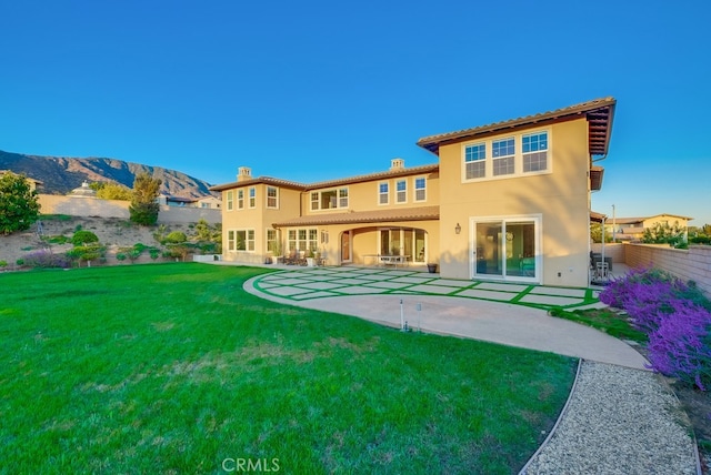 back of house with a lawn, a mountain view, and a patio