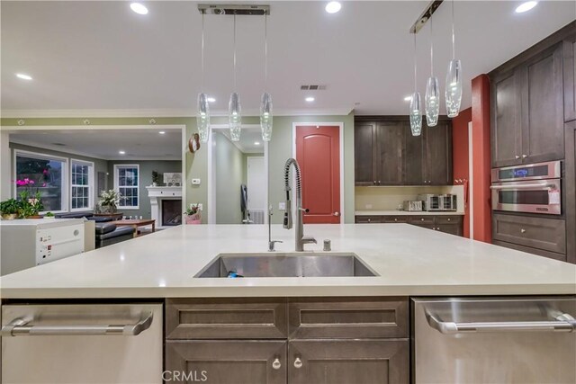 kitchen featuring decorative light fixtures, sink, stainless steel appliances, and a center island with sink