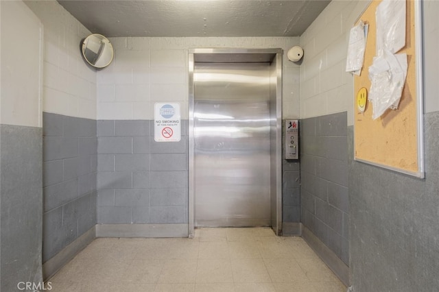 bathroom featuring elevator and tile walls