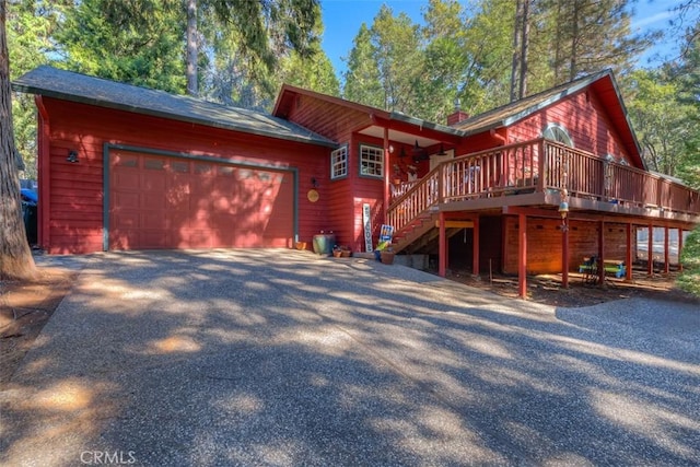 chalet / cabin featuring a wooden deck, stairway, aphalt driveway, a chimney, and an attached garage