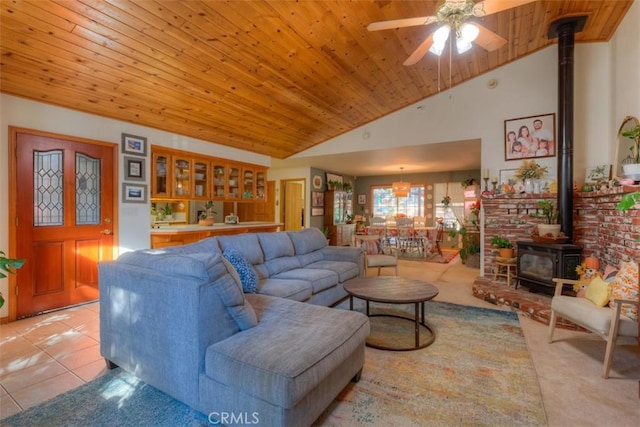 living area with light tile patterned flooring, ceiling fan, a wood stove, and wooden ceiling