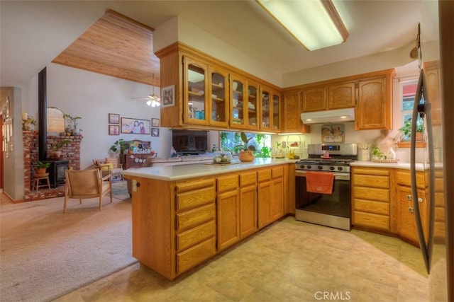 kitchen featuring glass insert cabinets, light countertops, under cabinet range hood, stainless steel gas range, and a peninsula