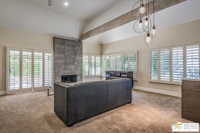 carpeted living room featuring lofted ceiling with beams, a wealth of natural light, a tile fireplace, and an inviting chandelier