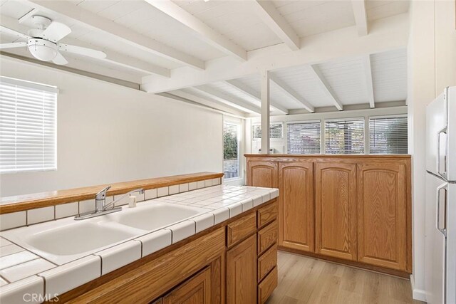 kitchen with tile counters, beam ceiling, light wood-type flooring, white fridge, and ceiling fan