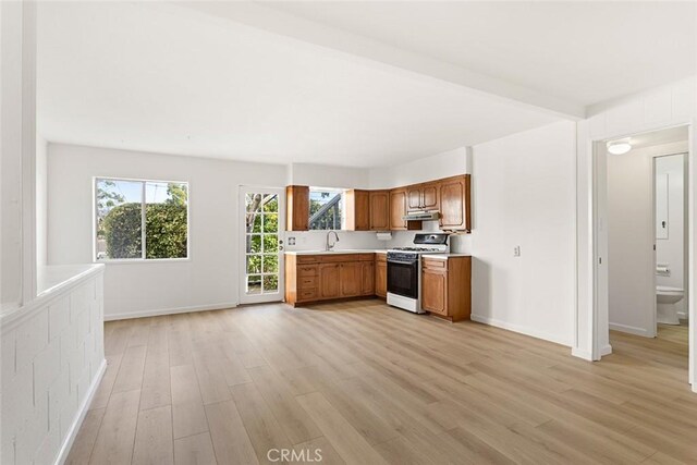 kitchen with white gas range, light hardwood / wood-style floors, beam ceiling, and sink