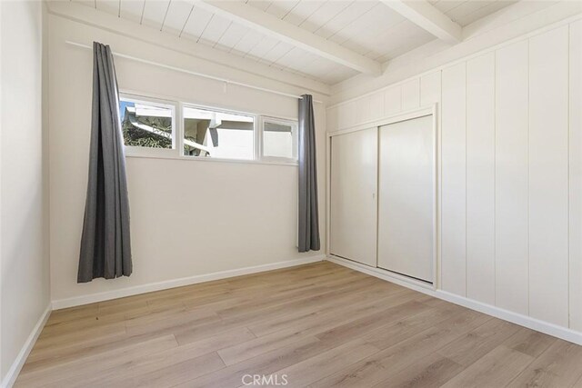 unfurnished bedroom featuring beam ceiling, wood ceiling, light wood-type flooring, and a closet