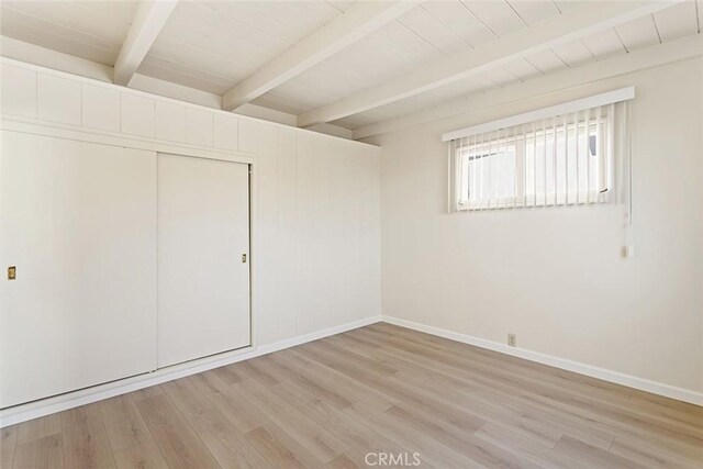 unfurnished bedroom with beamed ceiling, a closet, light wood-type flooring, and wooden ceiling