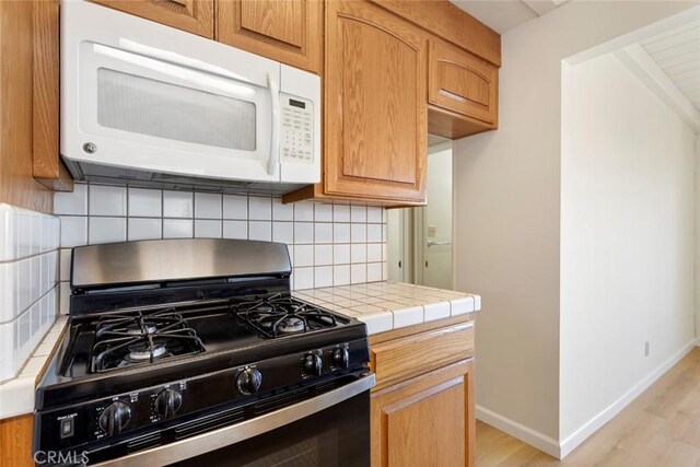 kitchen with light hardwood / wood-style floors, tile counters, decorative backsplash, and stainless steel gas stove