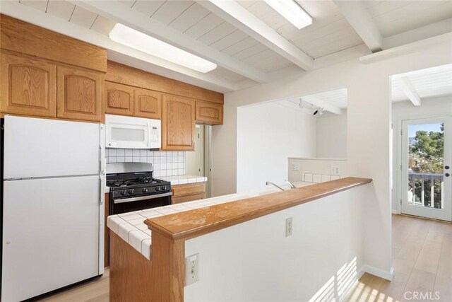 kitchen with white appliances, kitchen peninsula, light hardwood / wood-style floors, beamed ceiling, and tile counters